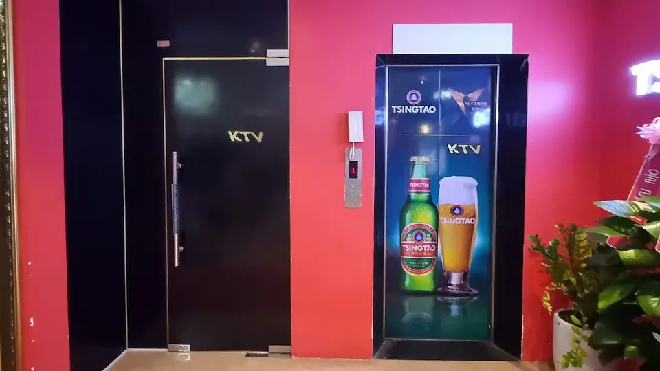 다낭 아우디 가라오케 핑크 벽면과 KTV 전용 블랙 도어, 칭따오 맥주 광고 디스플레이가 설치된 가라오케 입구