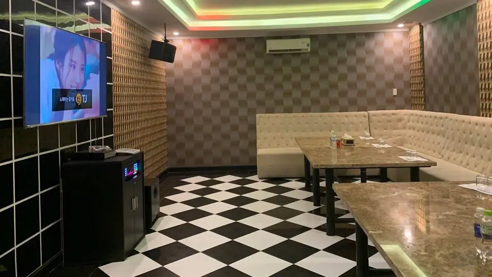 다낭 원오페라 가라오케 알록달록한 RGB LED 천장 조명과 TJ 노래방 기기, 크림색 소파 및 흑백 체크 바닥이 특징인 가라오케 룸