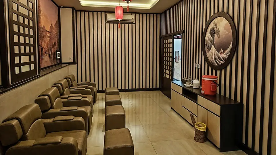 다낭 사쿠라 마사지 줄지어 배치된 갈색 가죽 리클라이너 의자와 풋 레스트, 붉은 홍등과 일본 수묵화로 장식된 풋 마사지 룸