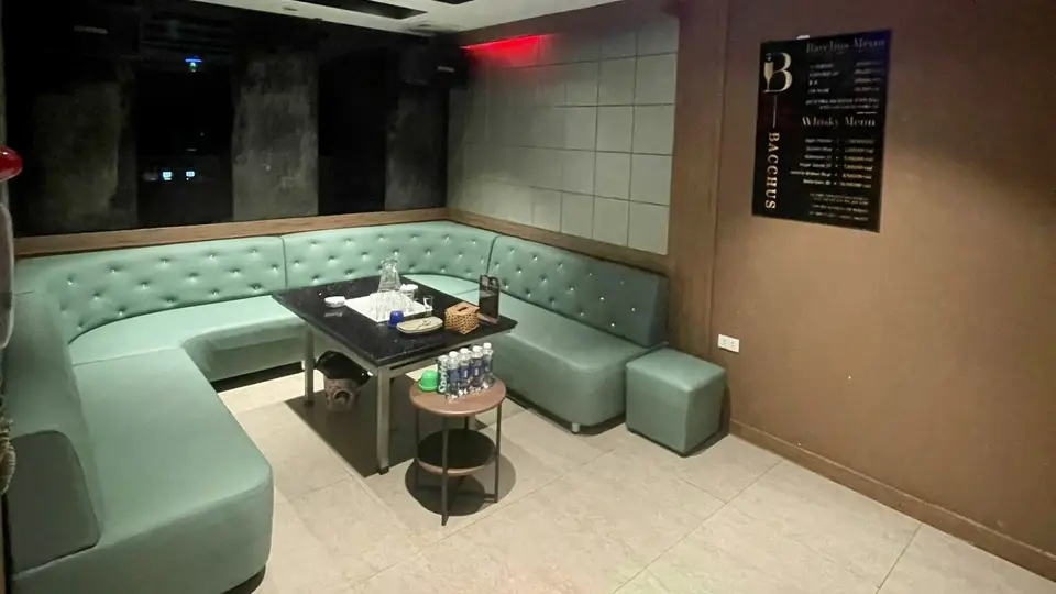 하노이 박카스 가라오케 민트 컬러 버튼 터프티드 U형 소파와 다크 그레이 패딩 벽, BACCHUS 메뉴판이 비치된 VIP 룸 내부
