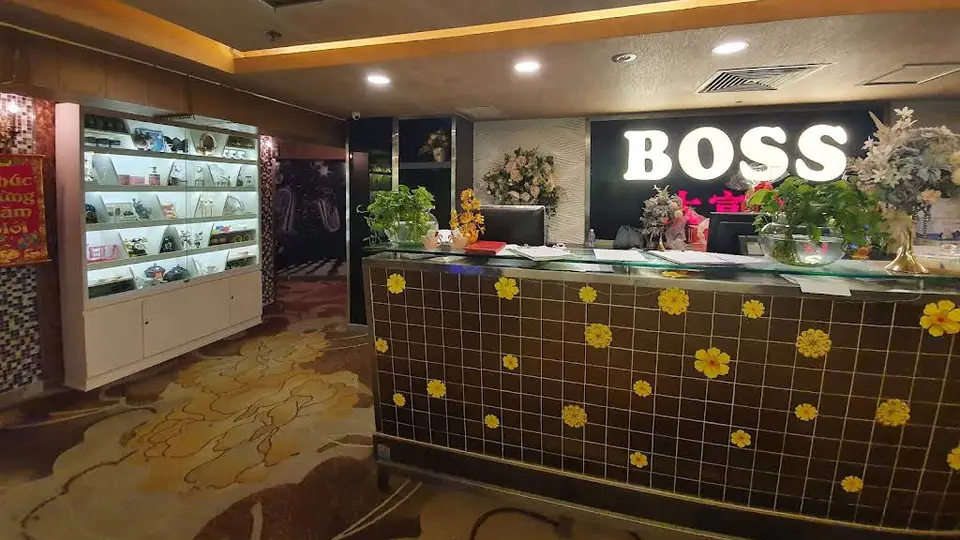 호치민 보스 가라오케 BOSS 로고 조명과 꽃 장식 타일 카운터, 진열장이 배치된 보스 가라오케의 메인 리셉션 전경