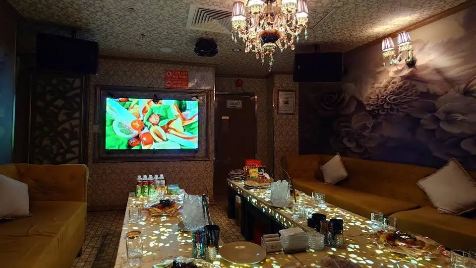 호치민 보스 가라오케 크리스탈 샹들리에 조명과 머스타드 색 소파, 플로럴 벽지가 갖춰진 가라오케 룸 내부