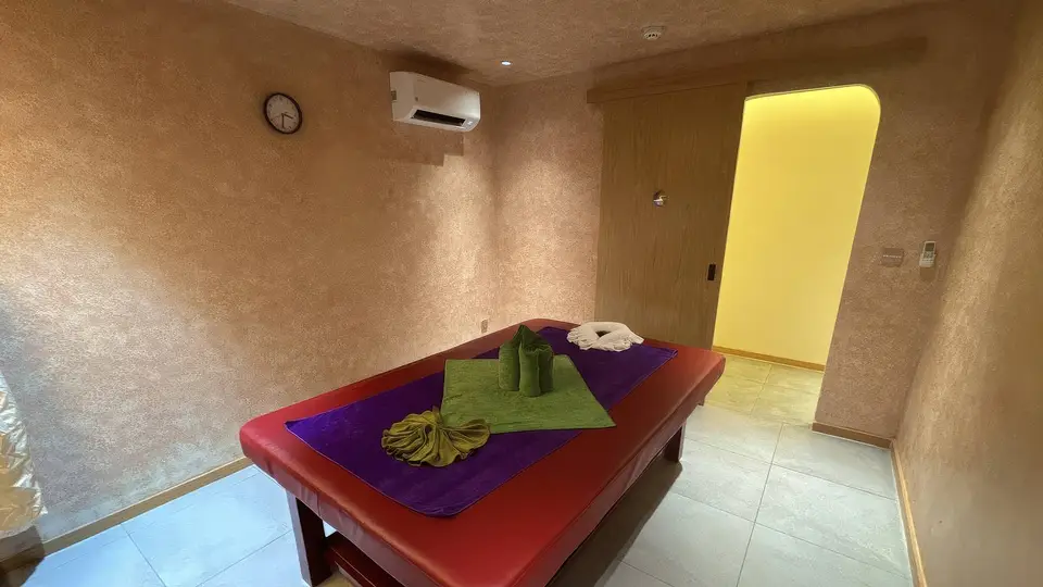 호치민 해피 마사지 황토빛 텍스처 벽면과 보라색·초록색 린넨이 세팅된 붉은 마사지 베드, 아치형 조명 출입구가 있는 스탠다드 룸