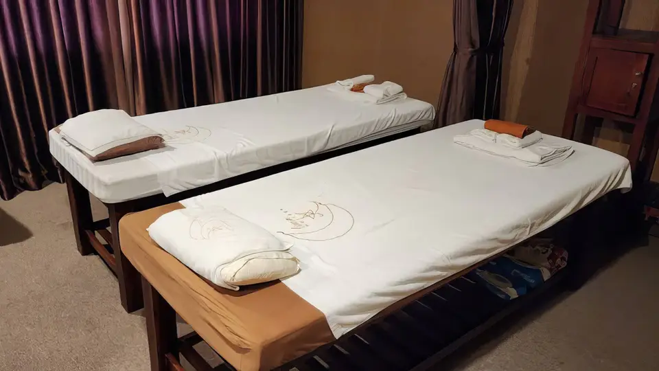 호치민 루나 마사지 루나 마사지 로고가 수놓인 흰 시트의 마사지 베드 두 개가 나란히 놓인 커플 전용 마사지 룸