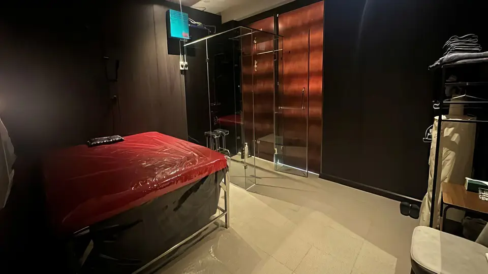 호치민 슈퍼맨 마사지 슈퍼맨 마사지 룸 내부 — 빨간 비닐 커버의 마사지 베드와 유리 파티션으로 구분된 샤워 공간, 어두운 우드 톤 벽면의 프라이빗 룸